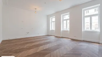Helles, geräumiges Zimmer mit elegantem Fischgrätparkett und hohen Fenstern, ideal für Wohnzwecke.