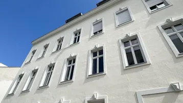 Fassade eines Altbaus mit vielen Fenstern und Rollläden unter blauem Himmel.