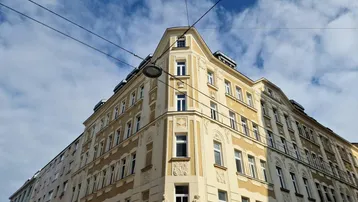 Eindrucksvolle Eckfassade eines Altbaus mit dekorativen Elementen unter blauem Himmel.