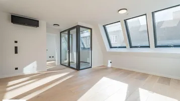Heller Wohnraum im Dachgeschoss mit schrägen Fenstern, Holzboden und moderner Klimaanlage.