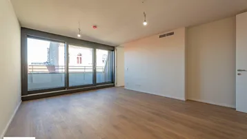 Helles, leeres Zimmer mit Holzboden und großen Schiebetüren, die Zugang zu einem Balkon bieten.