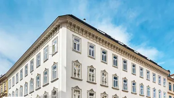 Klassische Altbaufassade mit eleganten Fensterrahmen und Stuckverzierungen unter blauem Himmel.