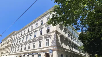 Klassisches Altbaugebäude mit eleganter Fassade und vielen Fenstern unter blauem Himmel.