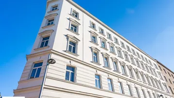 Weiße Fassade eines Altbaus mit vielen Fenstern und klassischer Architektur unter blauem Himmel.