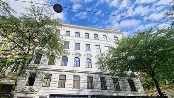 Klassisches Mehrfamilienhaus mit weißer Fassade und vielen Fenstern unter blauem Himmel.