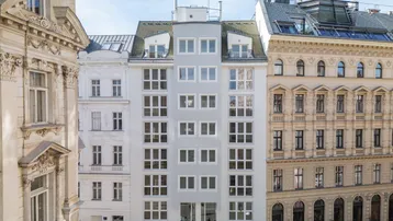 Modernes Wohngebäude mit vielen Fenstern, umgeben von historischen Altbauten in der Stadt.