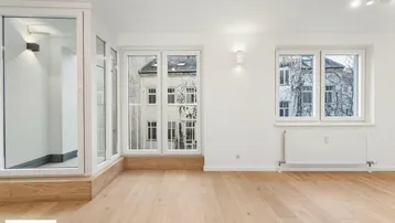 Helles Wohnzimmer mit Parkettboden, großen Fenstern und Zugang zu einem Balkon.