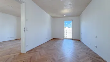 Heller Raum mit Fischgrätparkett, Holzbalkendecke und Zugang zu einem französischen Balkon.