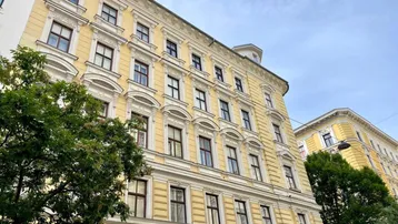 Historisches Gebäude mit gelber Fassade und reich verzierten Fenstern unter bewölktem Himmel.