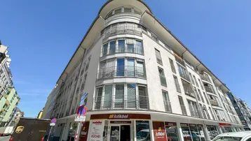 Mehrstöckiges Gebäude mit Geschäftsflächen im Erdgeschoss und Wohneinheiten darüber, unter klarem blauem Himmel.