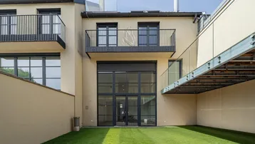 Moderne Gebäudefassade mit großen Fenstern, Balkonen und einer kleinen Rasenfläche im Hinterhof.