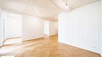 Geräumiger, heller Wohnbereich mit Holzbalkendecke, Fischgrätparkettboden und sichtbaren Holzbalken.