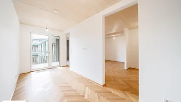 Heller Wohnbereich mit Fischgrätparkett und großen Fenstern zum Balkon.