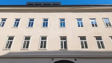 Die Fassade des Gebäudes zeigt eine Reihe von Fenstern und eine gepflegte, helle Außenansicht unter blauem Himmel.