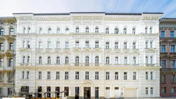 Weißes, historisches Gebäude mit reich verzierter Fassade und vielen Fenstern unter blauem Himmel.