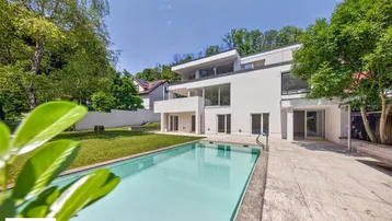 Moderne Villa mit großem Garten und integriertem Pool unter blauem Himmel.