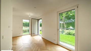 Helles Zimmer mit Fischgrätparkettboden und Zugang zu einem privaten Gartenbereich.