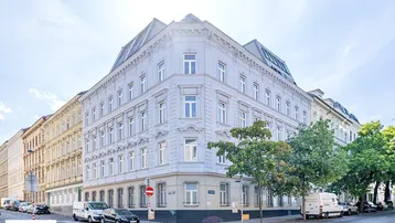 Historisches Eckgebäude in städtischer Umgebung mit klassischer Architektur und vielen Fenstern.