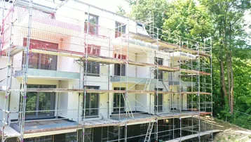 Neubauwohnung im Bauzustand mit Gerüst und Sicherheitsnetzen, umgeben von Bäumen.