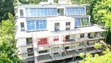 Neubauwohnhaus im Bauzustand mit Gerüst und Dachfenstern, umgeben von viel Grün.