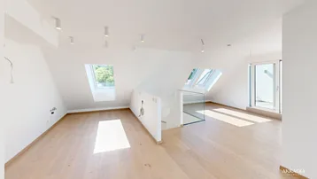 Heller, offener Wohnbereich im Dachgeschoss mit Holzboden, Dachfenstern und moderner Glasbrüstung.