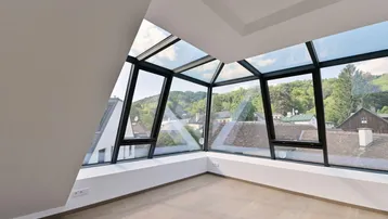 Heller Raum im Dachgeschoss mit großen Glasflächen und weitem Blick ins Grüne.