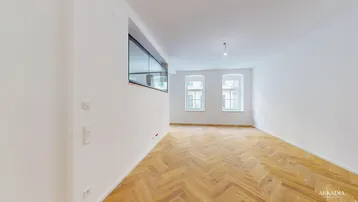 Heller, leerer Wohnraum mit Fischgrätparkett, hohen Fenstern und moderner Glasabtrennung.