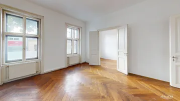 Helles Zimmer mit Fischgrätparkettboden, hohen Decken und großen Fenstern in einem Altbau.