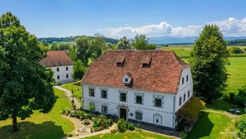 Historisches Anwesen mit weitläufigen Grünflächen und ländlicher Umgebung unter blauem Himmel.