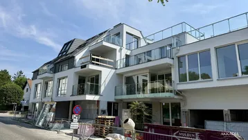 Modernes Mehrfamilienhaus im Bau mit großen Fenstern und Balkonen, umgeben von Baustellenmaterial.