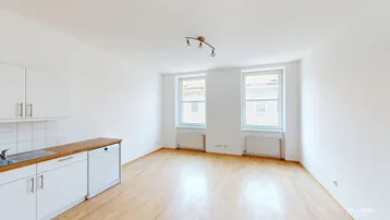 Heller offener Wohnbereich mit integrierter Küche, Holzboden und zwei Fenstern für viel Tageslicht.