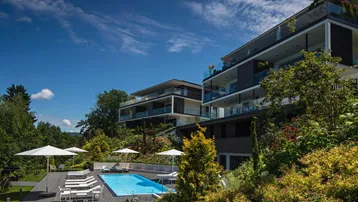 Moderne Apartmentgebäude mit Gemeinschaftspool, Holzdeck und Liegebereich unter blauem Himmel.