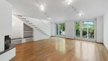 Helles Wohnzimmer mit Parkettboden, Kamin und großen Fenstern mit Blick ins Grüne.