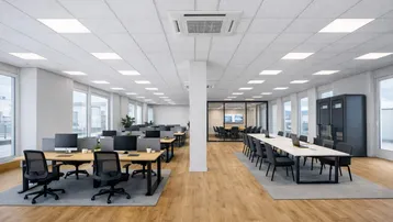 Modernes Großraumbüro mit zahlreichen Arbeitsplätzen, Konferenztisch und separatem Besprechungsraum, ausgestattet mit großen Fenstern und Holzfußboden.