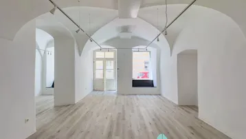 Heller, leerer Geschäftsraum mit Gewölbedecken, modernen Lichtschienen und hellem Laminatboden.