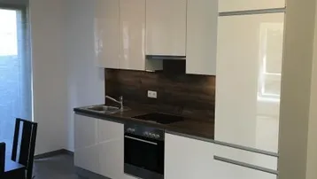 Moderne Küche mit weißen Hochglanzfronten, integrierten Geräten und Fliesenboden.