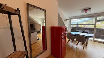 Heller offener Wohn- und Essbereich mit Holzboden, großem Spiegel und Zugang zum Balkon.
