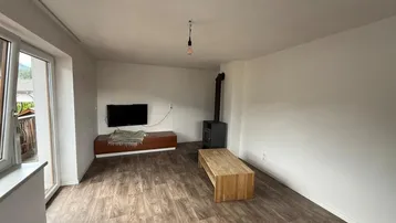 Helles Wohnzimmer mit Laminatboden, Kaminofen und Zugang zu einem Balkon.