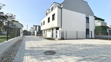 Modernes Reihenhaus mit weiß-grauer Fassade und gepflastertem Stellplatzbereich vor dem Gebäude.
