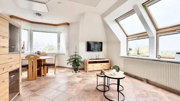 Heller Wohn- und Essbereich mit Fliesenboden, Dachfenstern und Blick ins Grüne.