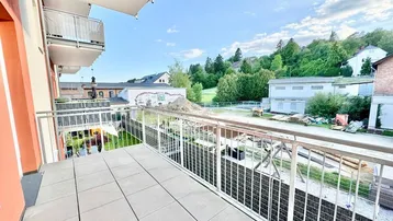 Geräumiger Balkon mit Fliesenboden und Blick auf die grüne Umgebung und angrenzende Gebäude.