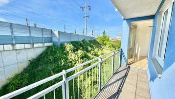 Geräumiger Balkon mit Blick auf eine begrünte Lärmschutzwand und Bahngleise unter blauem Himmel.