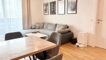 Helles Wohn- und Esszimmer mit modernem Sofa, Esstisch und Parkettboden.