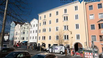 Gelbes historisches Gebäude mit vielen Fenstern und einem Torbogen an einer belebten Stadtstraße.