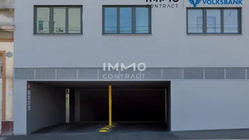 Moderne Gebäudefassade mit großen Fenstern und Zufahrt zur Tiefgarage.
