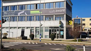Modernes Bürogebäude mit großen Fensterfronten und Werbeschildern an einer belebten Straße.