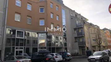 Mehrstöckiges Wohngebäude mit Geschäften im Erdgeschoss und parkenden Autos auf der Straße.