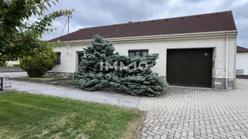 Einfaches Haus mit Garage, gepflasterter Einfahrt und Vorgarten unter bewölktem Himmel.