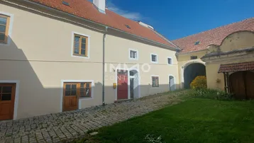 Historisches Gebäude mit gepflastertem Hof und grüner Rasenfläche unter blauem Himmel.