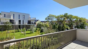 Blick vom Balkon auf den gepflegten Gemeinschaftsgarten und moderne Wohngebäude.